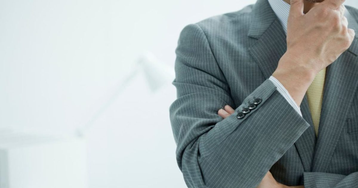 顎に手を当てるグレースーツを着た男性