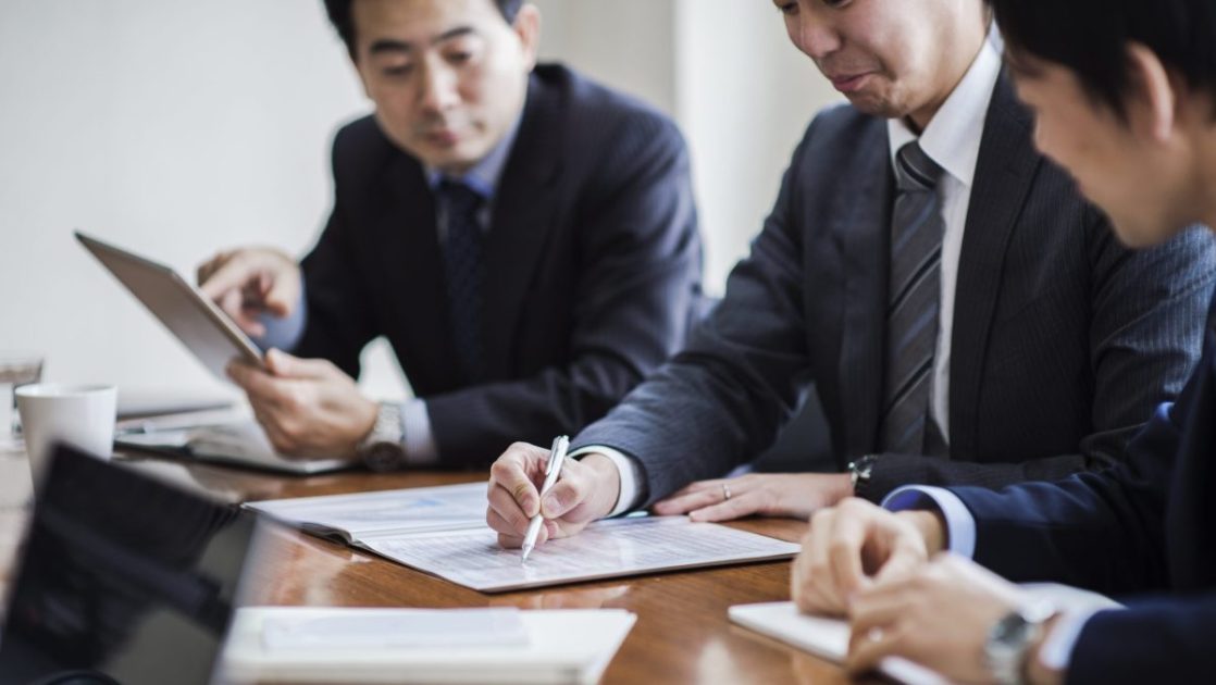 資料を見て話し合っている中年のビジネスマン三人