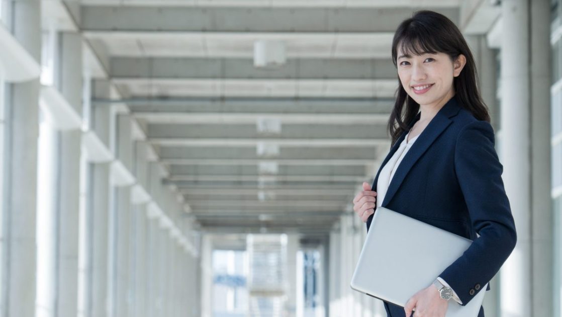 パソコンを手に持って立つスーツ姿の女性