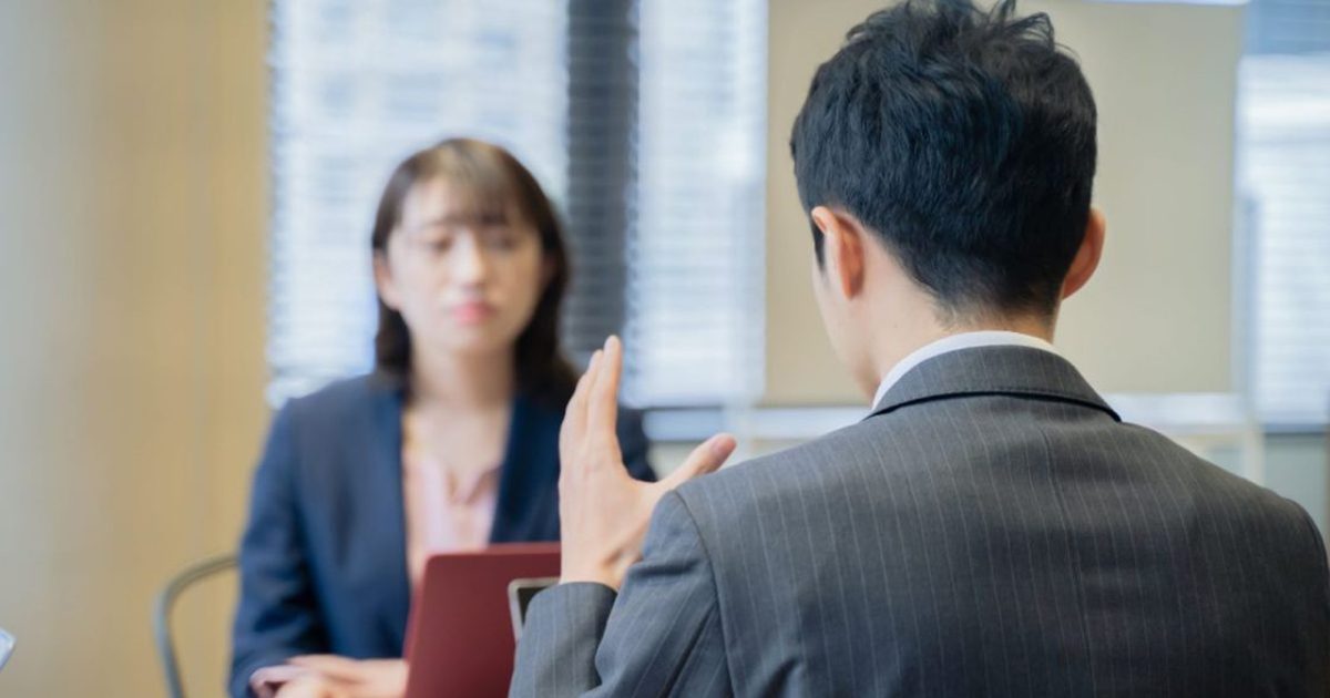 パソコンを見ながら向かいに座る女性に説明をするビジネスマン