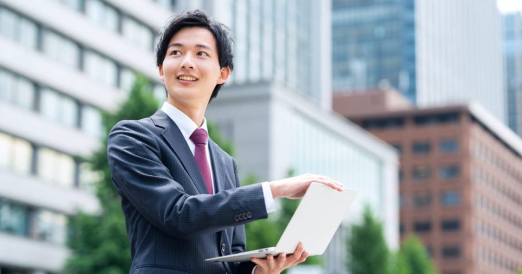 オフィス街でパソコンを開くスーツを着た男性