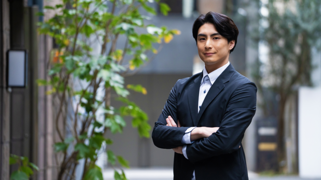腕を組んでこちらを見ているスーツ姿の男性