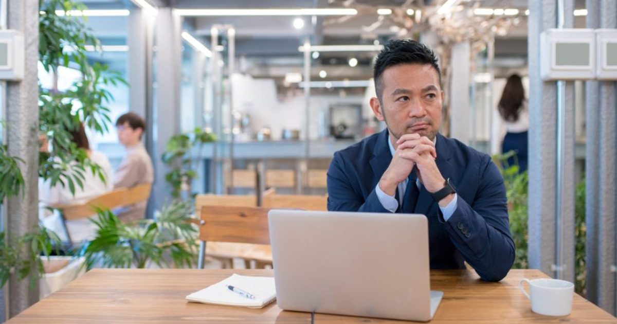 ノートパソコンを開いて顎に手を当てる男性