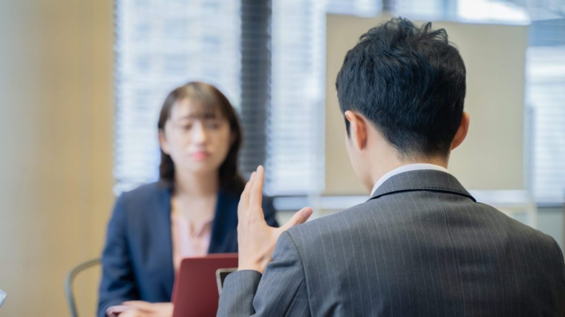 ジェスチャーをしながら女性に向かって話すスーツ姿の男性