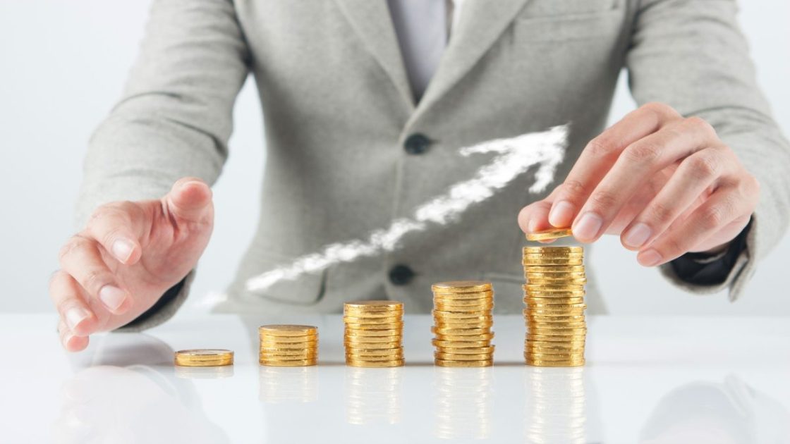 グレーのスーツを着た人が金色のコインを積み重ねる様子