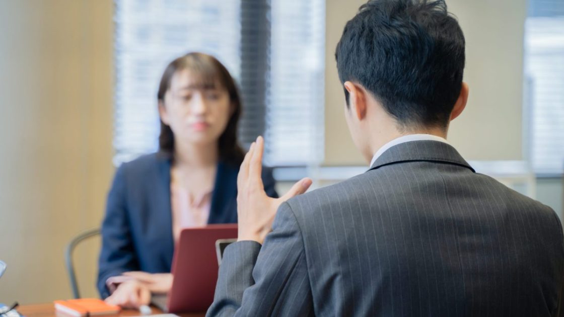 ジェスチャーをしながら女性に向かって話すスーツ姿の男性