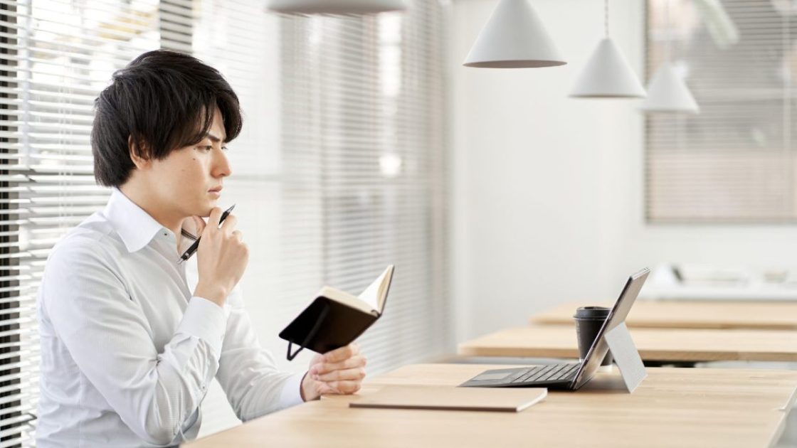 顎に手を当てて手帳を読む男性
