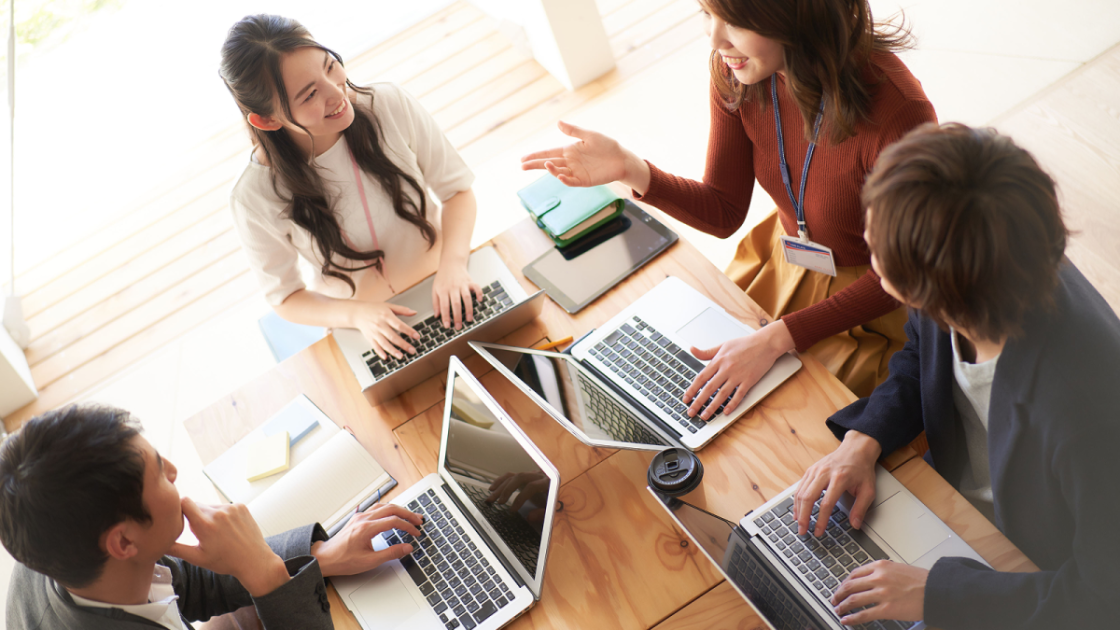 ノートパソコンを操作しながら話し合う4人の男女