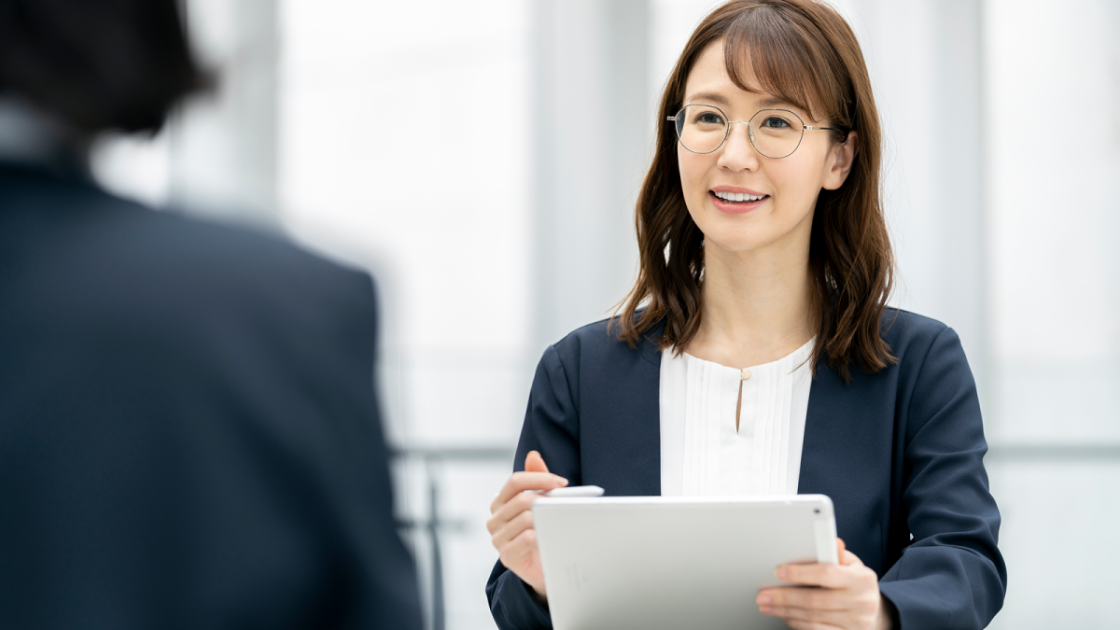 バインダーを持ちながら話すスーツ姿の女性