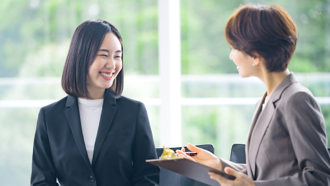 バインダーを片手に話すスーツを着た女性