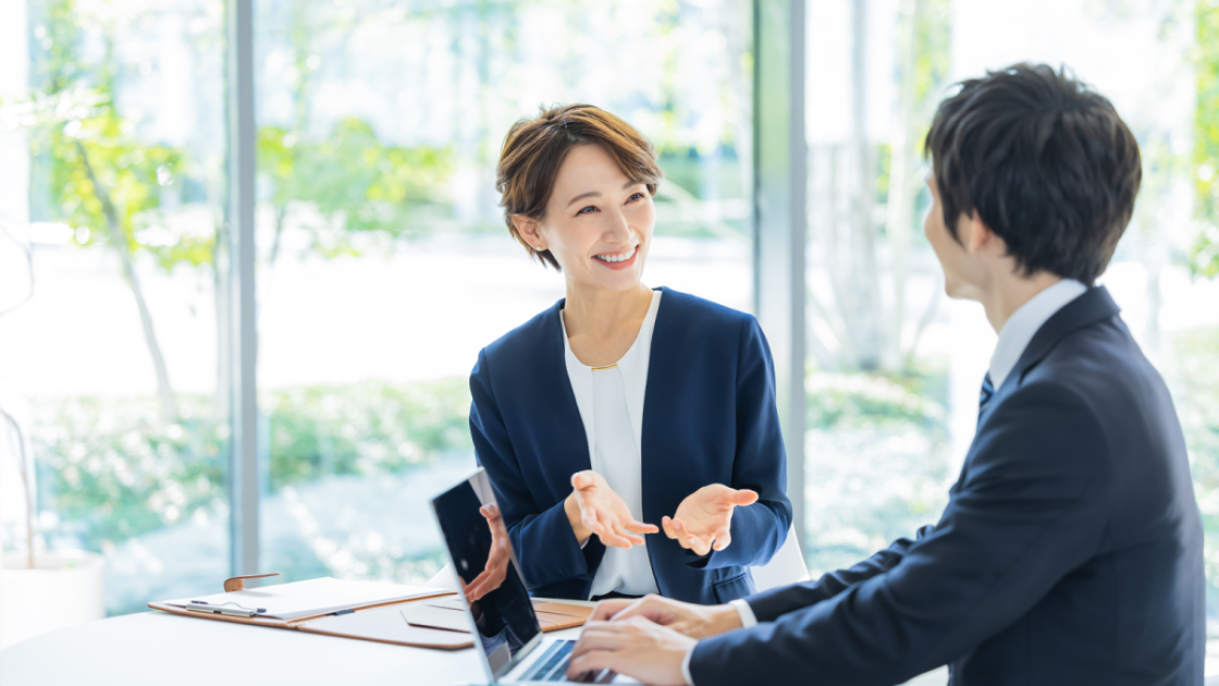 パソコンを操作するビジネスマンに話しかける女性