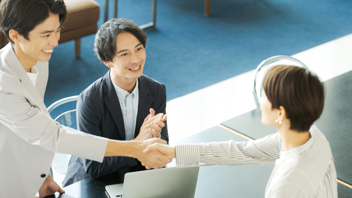 テーブル越しに握手をするスーツ姿の男女