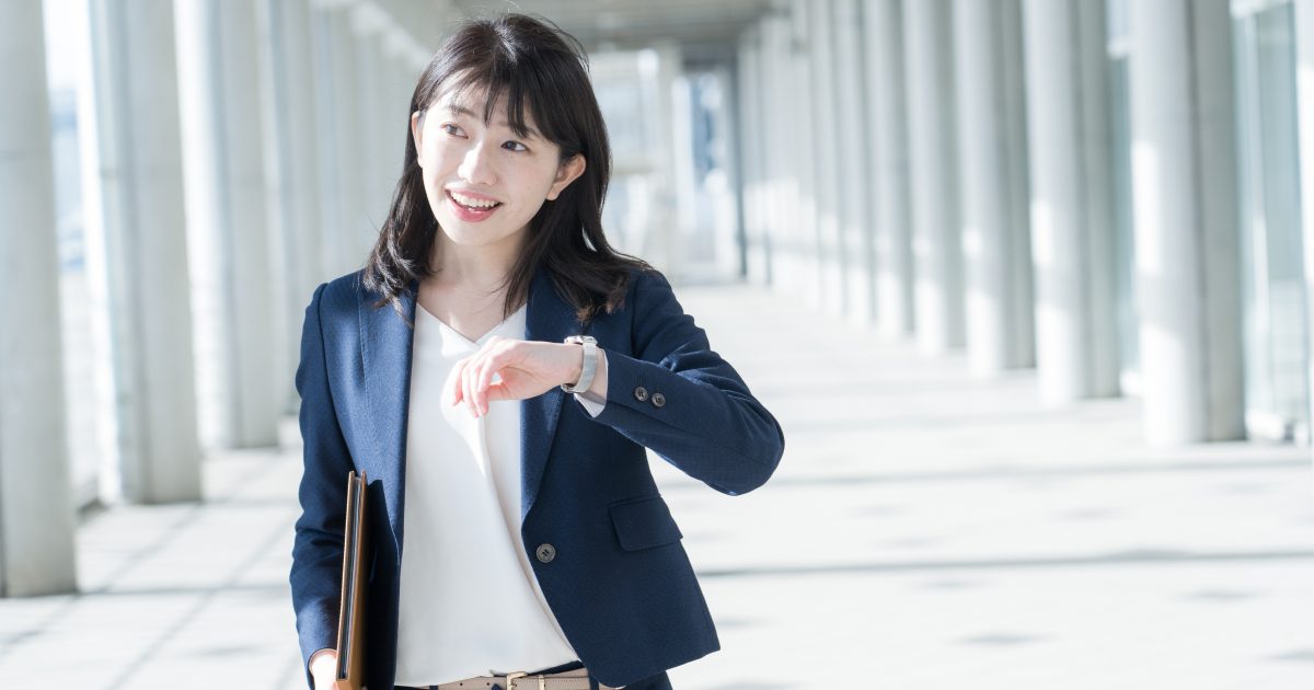 腕時計を見ながら歩くスーツ姿の女性