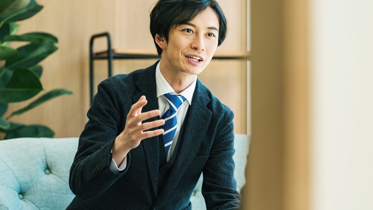 右手を動かしながら話すスーツ姿の男性
