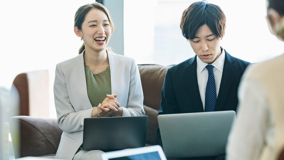膝にノートパソコンを置いて話し合う男女