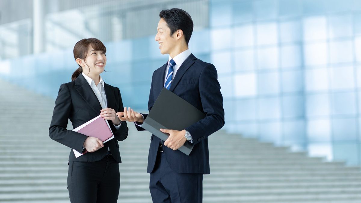 資料やノートパソコンを持ったまま話すスーツ姿の男女
