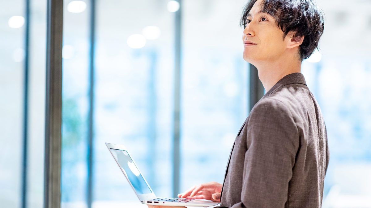 立ちながらノートパソコンを操作する男性
