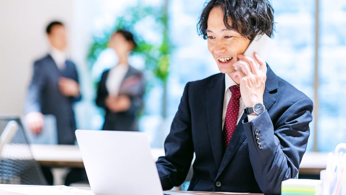 A man talking on a smartphone while operating a laptop