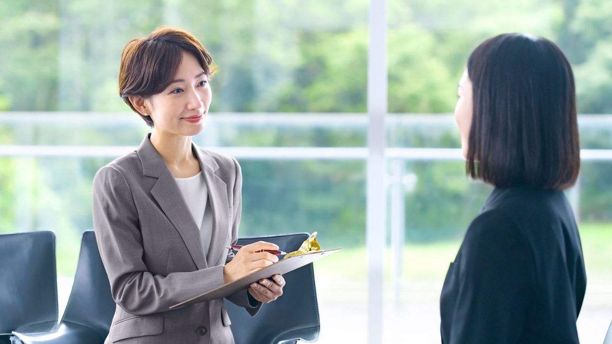 A woman taking notes on paper in a binder while listening to the other person