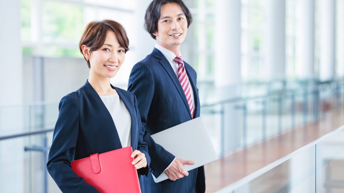 ノートパソコンを持って並んで立つ男女