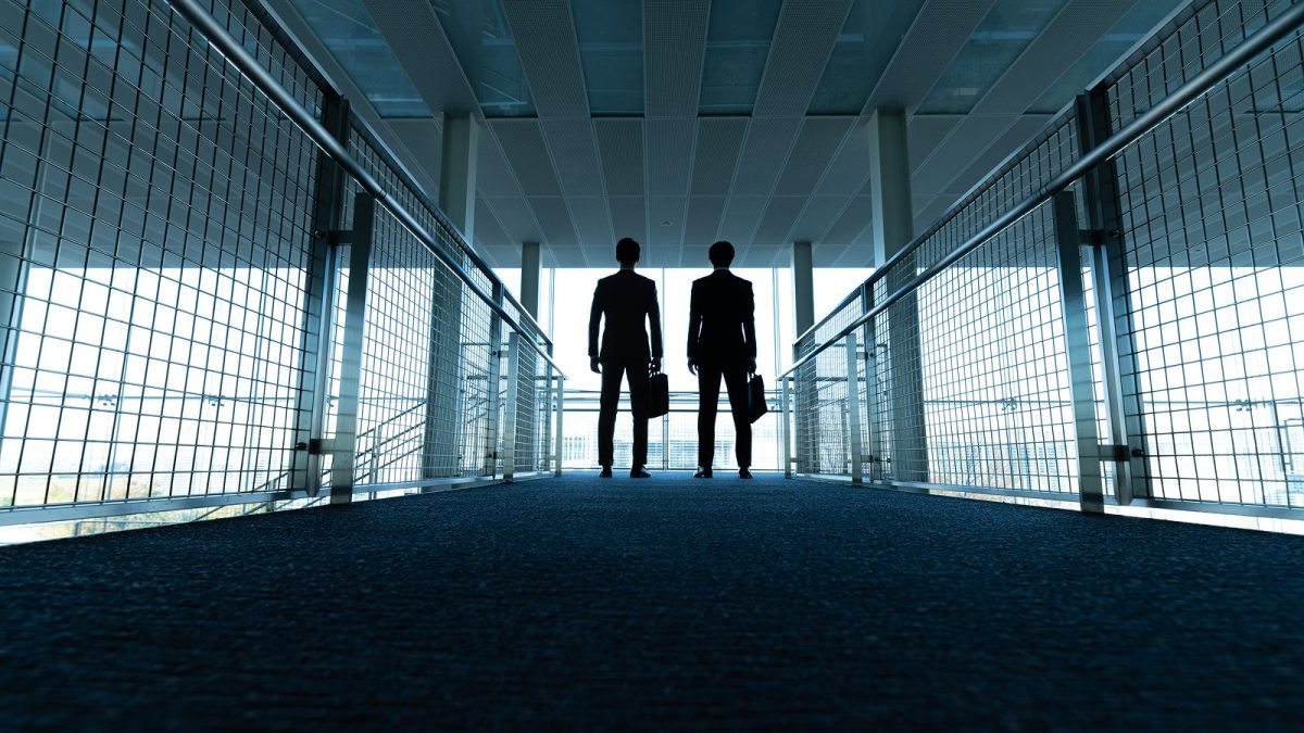 The back view of a businessman in a suit walking down a hallway