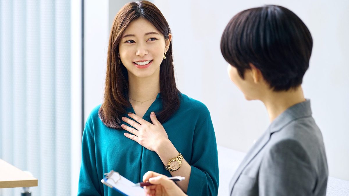 バインダーにメモをとる女性と胸に手を当てて話す女性