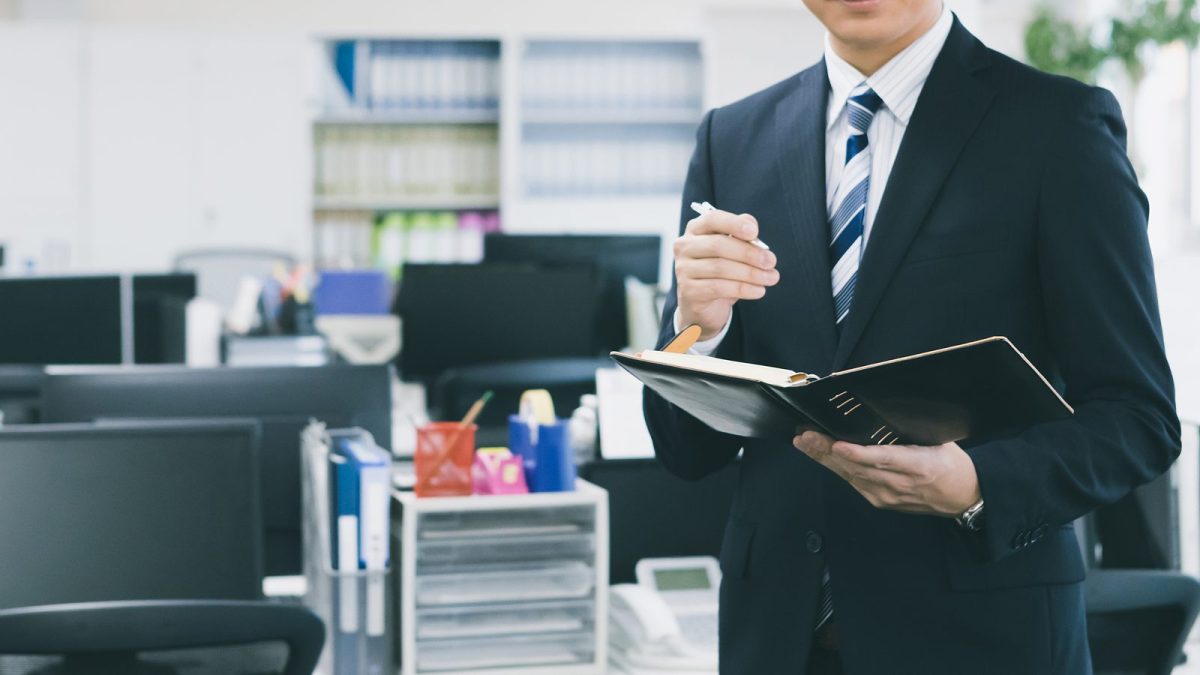 立ったままノートにメモを取るスーツ姿の男性