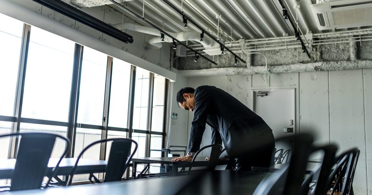 オフィスのデスクに両手をついて項垂れる男性