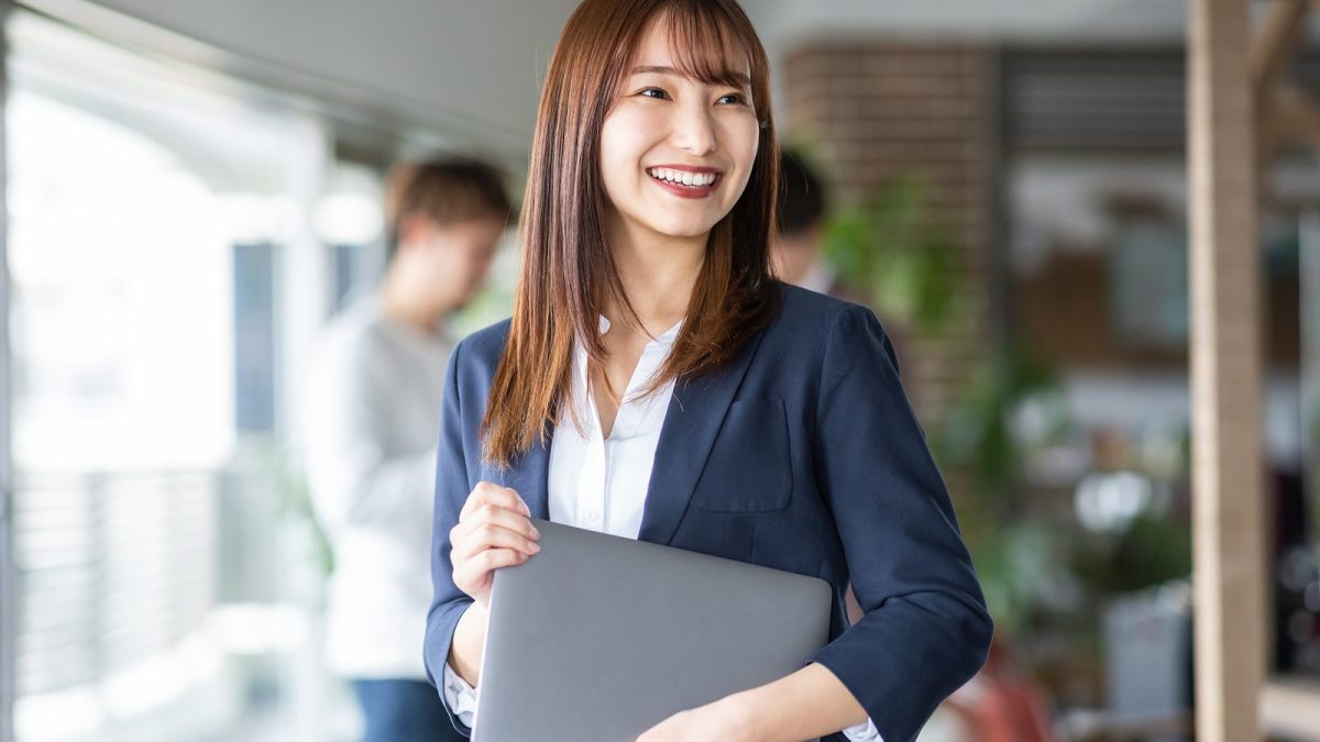 ノートパソコンを持って微笑む若い茶髪の女性