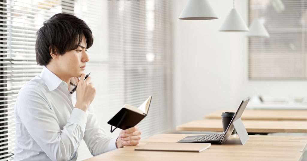 顎に手を当ててノートを開く男性