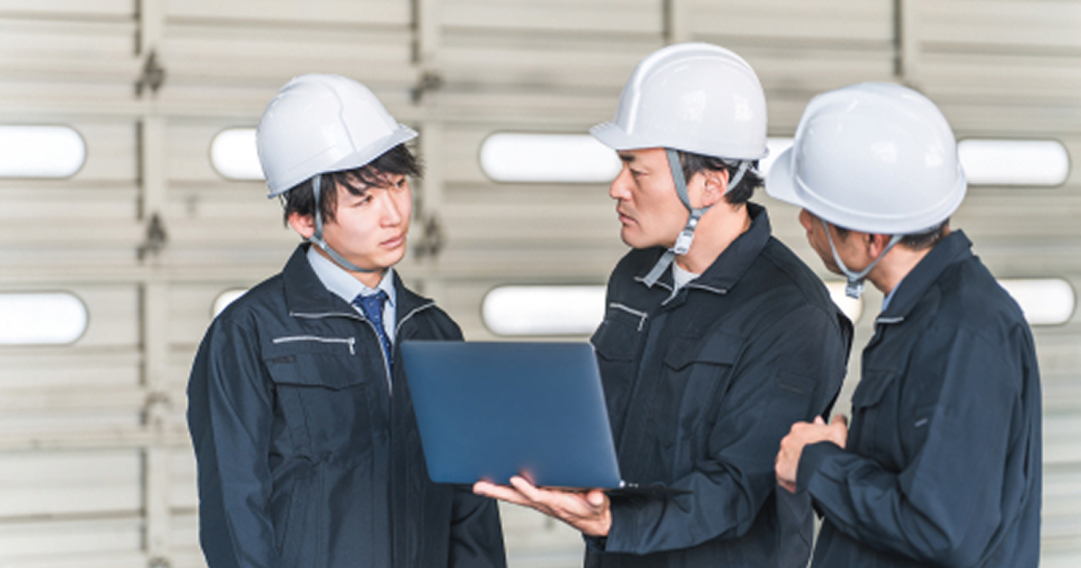建設現場でノートパソコンを開き話し合う3人の男性