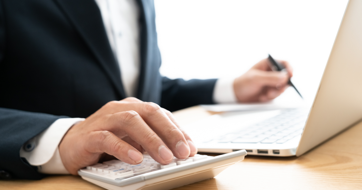 ノートパソコンを見ながら電卓を叩く男性