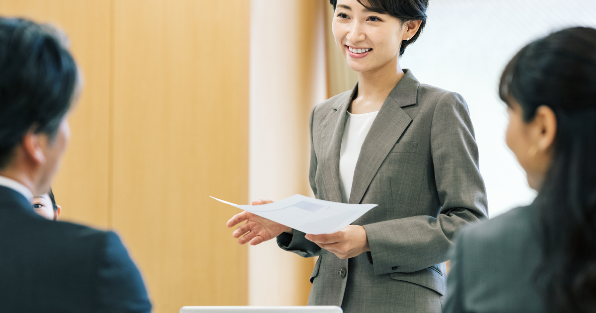 紙の資料を持ってプレゼンをする女性