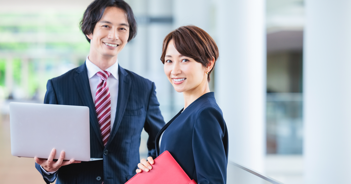 ノートパソコンを持って立つスーツ姿の男女