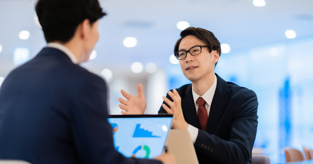 ノートパソコンを開いて資料の説明をするスーツ姿の男性