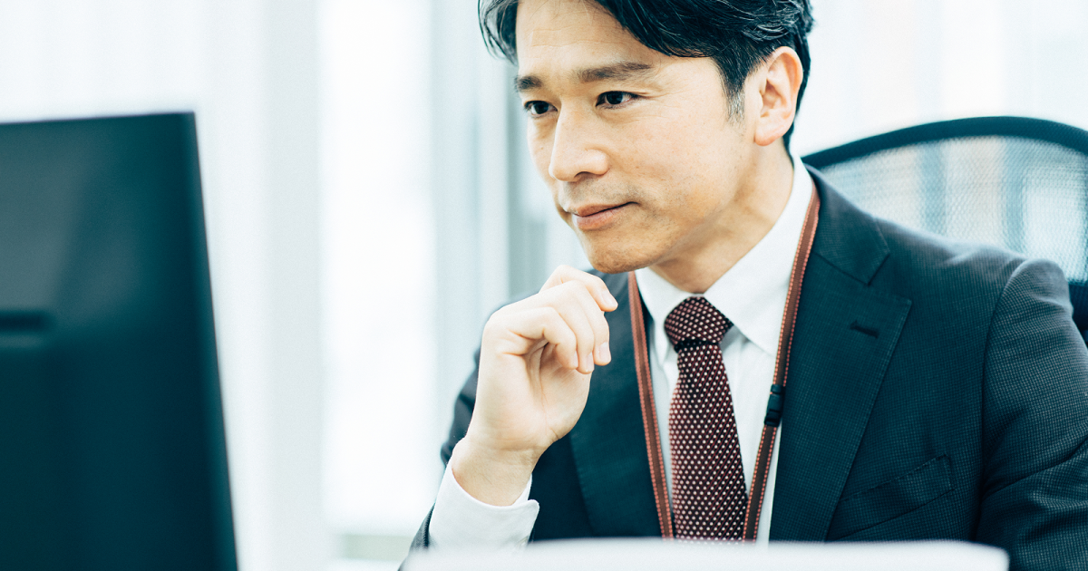 顎に手を当てながらパソコンの画面を見る男性