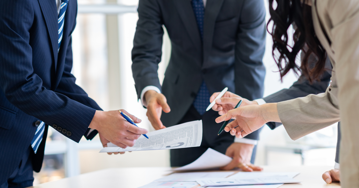 ボールペンを持ったまま紙の資料を指さす様子