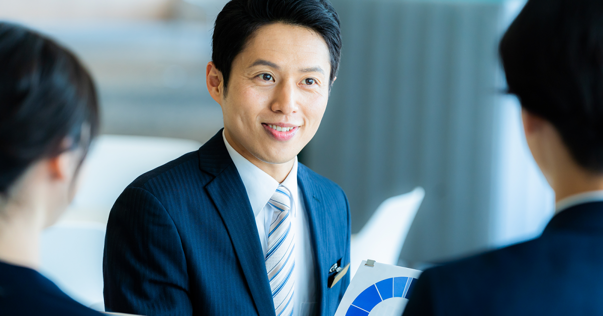 紙の資料を商談相手に見せる男性