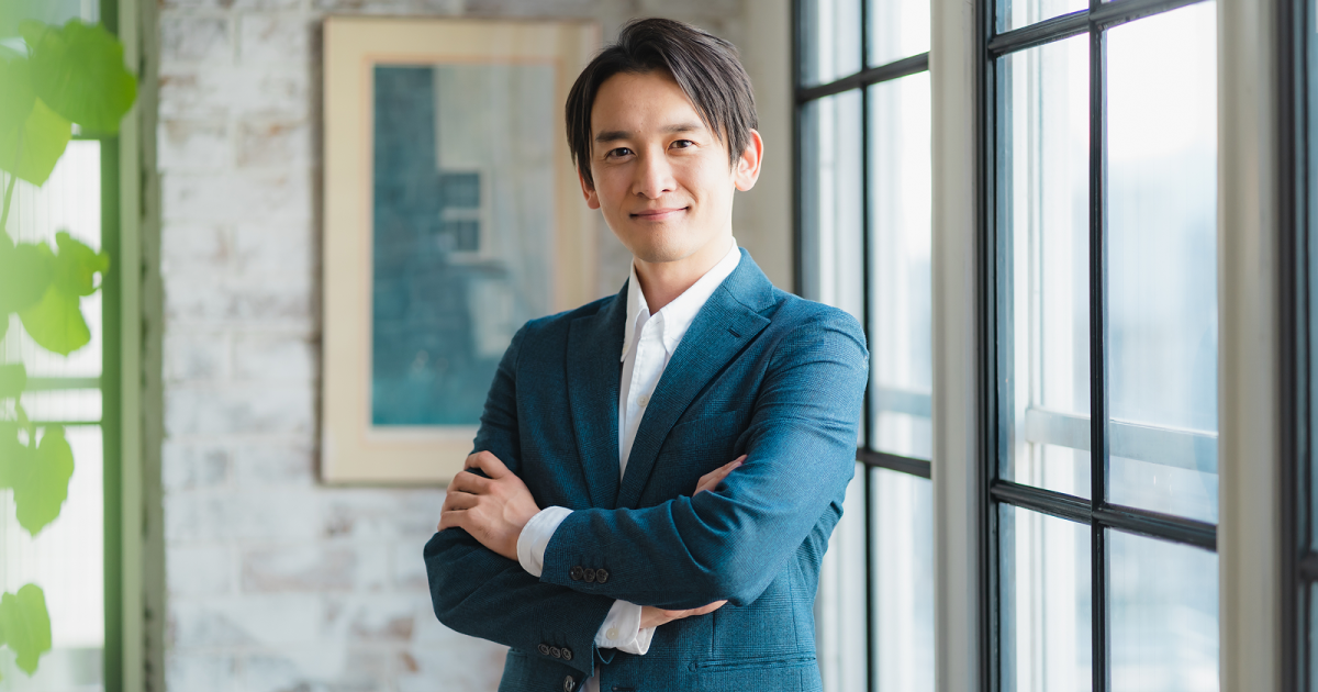 腕を組んで立つスーツ姿の男性