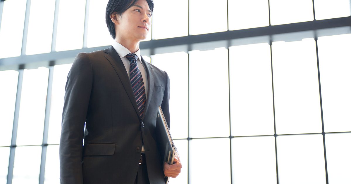ノートパソコンを脇に抱えてオフィスを歩く男性