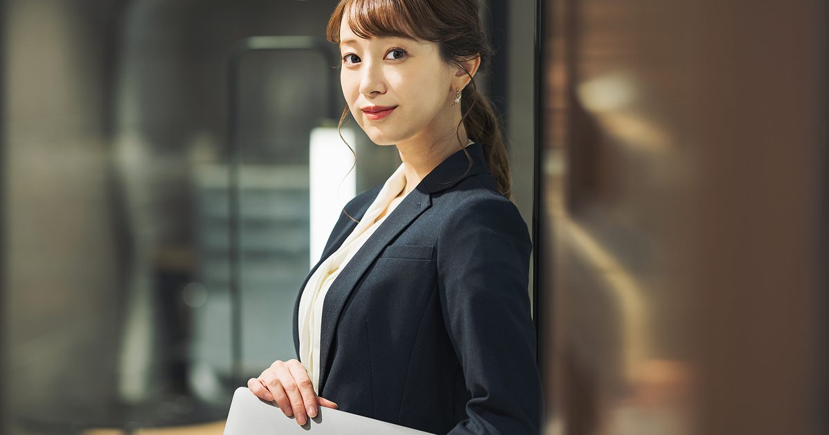 ノートパソコンを小脇に抱えて立つ女性