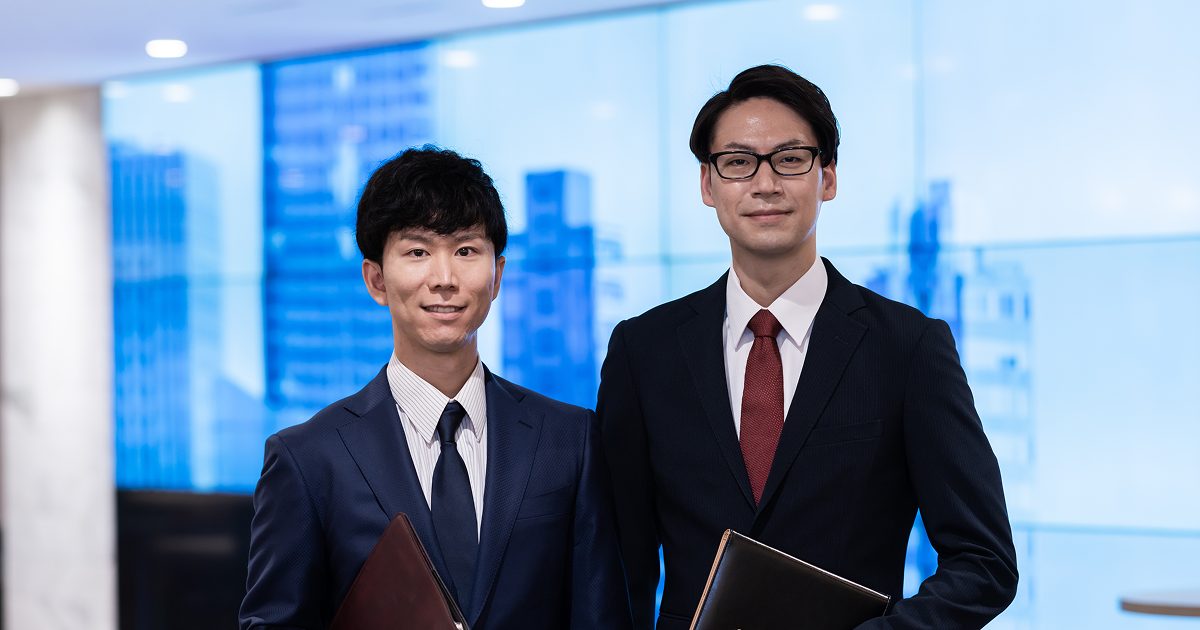 執務室で並んで立つスーツ姿の男性二人