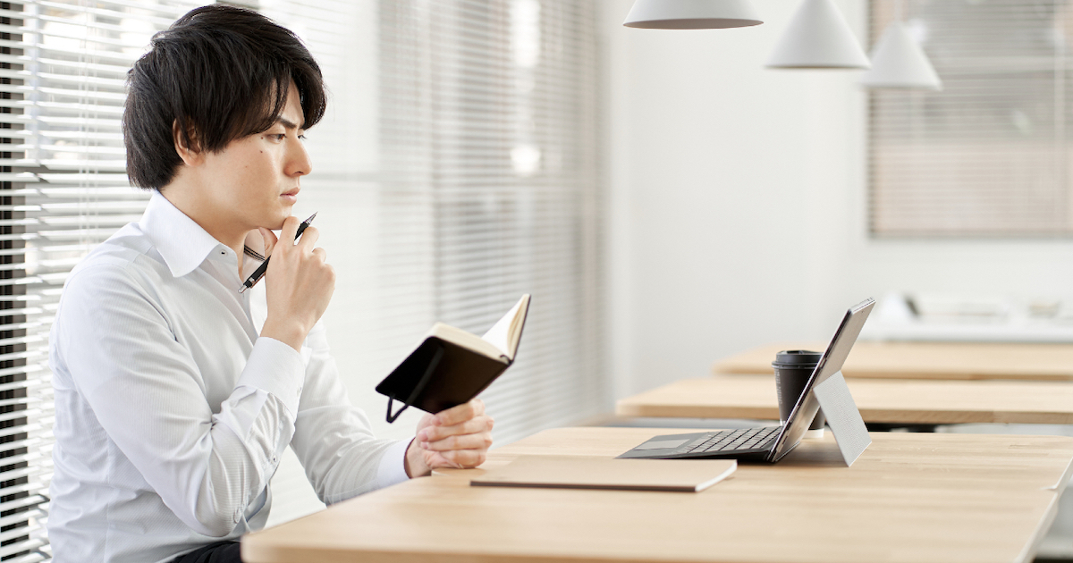 顎に手を当ててメモ帳を見る男性