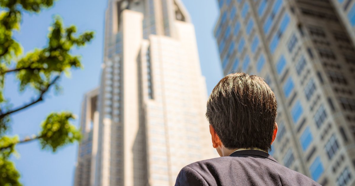 オフィスビルを見上げる男性の後ろ姿