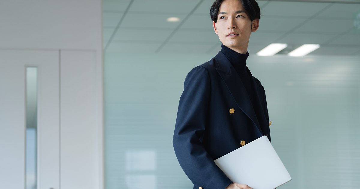 パソコンを脇に抱えて立つ若い男性