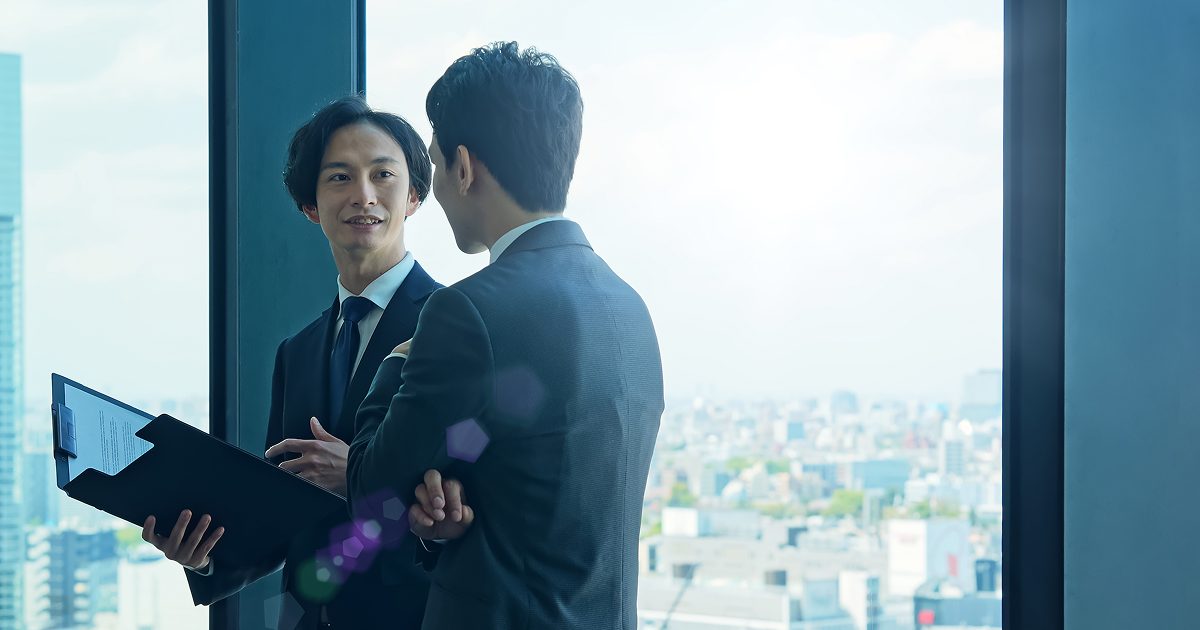 バインダーに挟んだ紙の資料を片手に話し合う男性