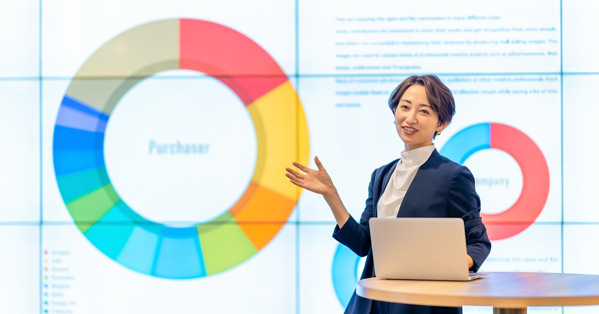 モニターに資料を映してプレゼンをするスーツ姿の女性