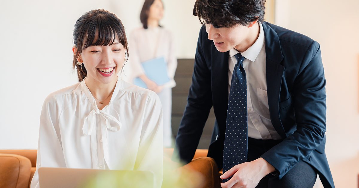 笑顔でパソコンを操作する女性とスーツ姿の男性