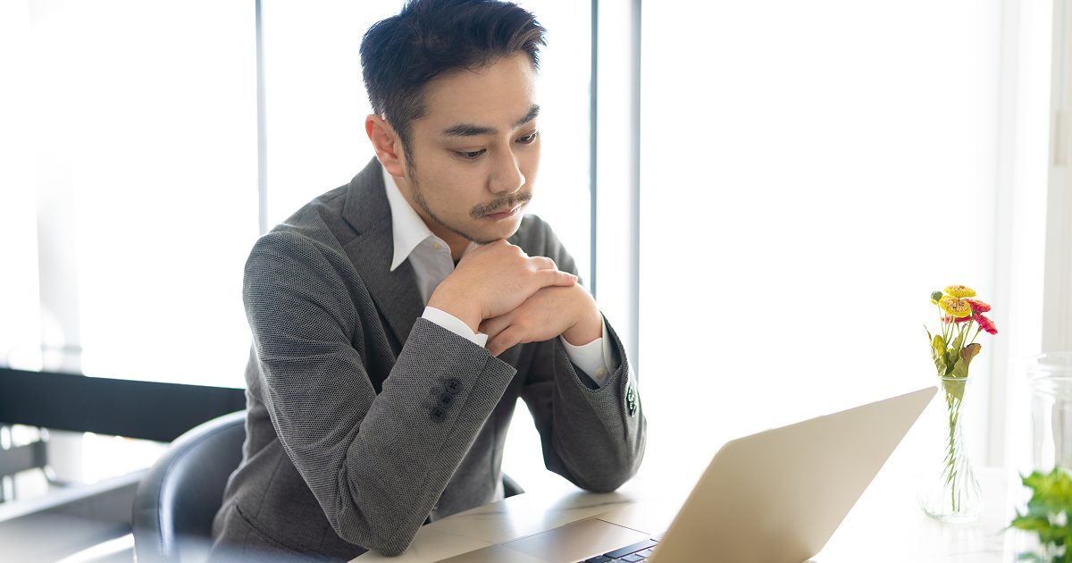 腕を組んでパソコンを見る男性