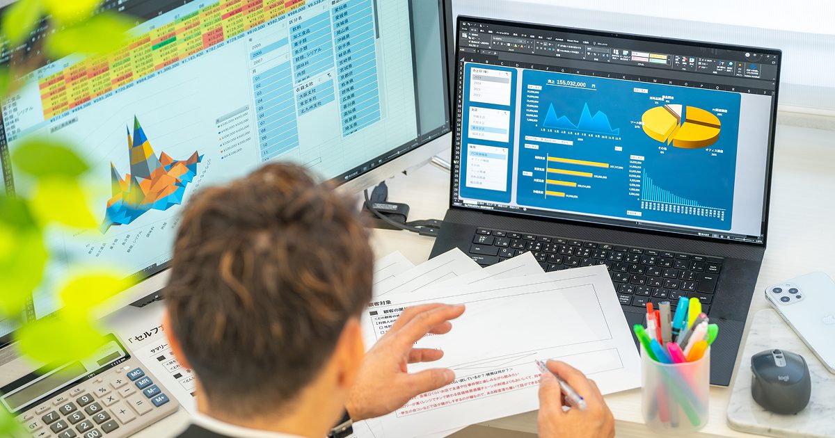 複数のデータを見比べて分析をする男性の後ろ姿